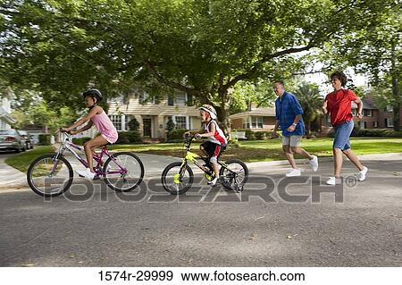 Children riding bicycle on the road while parents running behind them View Large Photo Image Stock Photo - Children riding bicycle on the road while parents running behind them. Fotosearch