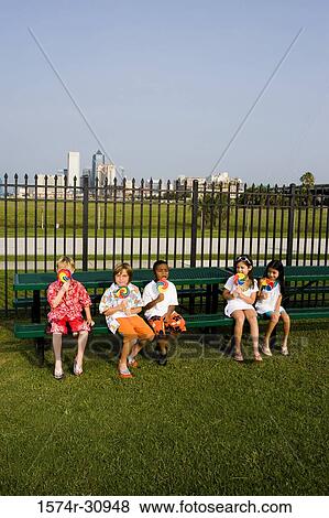 Children sitting on a bench by the fence and having lollipops View Large Photo Image Stock Photo - Children sitting on a bench by the fence and having lollipops. Fotosearch