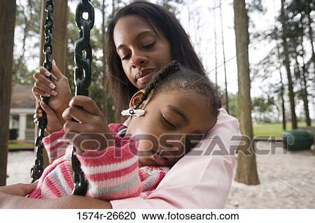 Stock Image - Close-up of a daughter sleeping in her mother's arms at park. Fotosearch