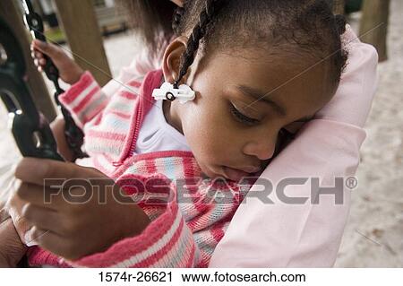 Stock Image - Close-up of a daughter sleeping in her mother's arms at park. Fotosearch