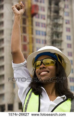 Close-up of a female architect wearing hardhat with arm raised and smiling View Large Photo Image Stock Photo - Close-up of a female architect wearing hardhat with arm raised and smiling. Fotosearch
