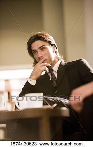 Contemplative businessman sitting by table in an office View Large Photo Image Stock Image - Contemplative businessman sitting by table in an office. Fotosearch