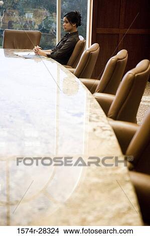 Picture - Contemplative businesswoman sitting by conference table with hands clasped in an office. Fotosearch