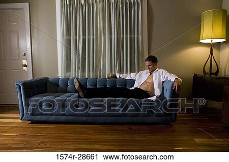 Contemplative mid adult man holding a glass while sitting on sofa View Large Photo Image Stock Image - Contemplative mid adult man holding a glass while sitting on sofa. Fotosearch