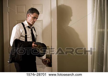 Stock Image - Contemplative mid adult man with hat standing by a door. Fotosearch