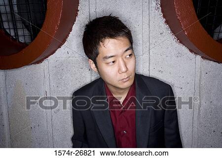 Stock Image - Contemplative young businessman leaning by wall. Fotosearch