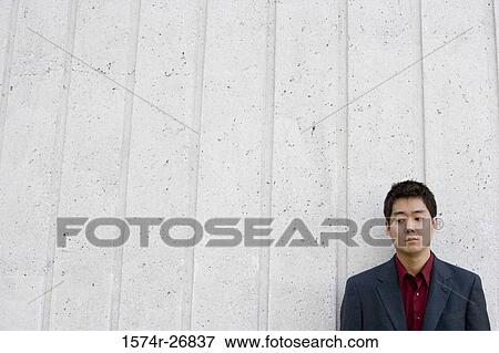 Stock Photo - Contemplative young businessman leaning by wall. Fotosearch