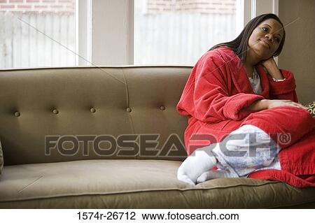 Stock Image - Contemplative young woman in gown sitting on a sofa. Fotosearch