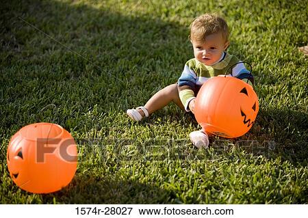 Stock Photo - Cute boy playing with pumpkin Halloween bag on grass. Fotosearch