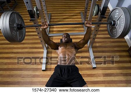 Elevated view of a young man bench-pressing barbell in the gym View Large Photo Image Stock Image - Elevated view of a young man bench-pressing barbell in the gym. Fotosearch