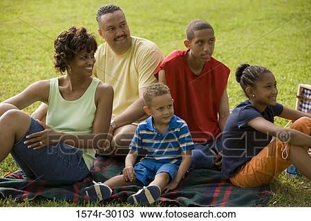 Stock Image - Family sitting on blanket at park. Fotosearch