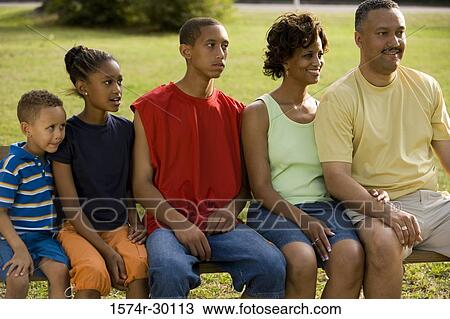Stock Image - Family sitting side by side on the bench at park. Fotosearch