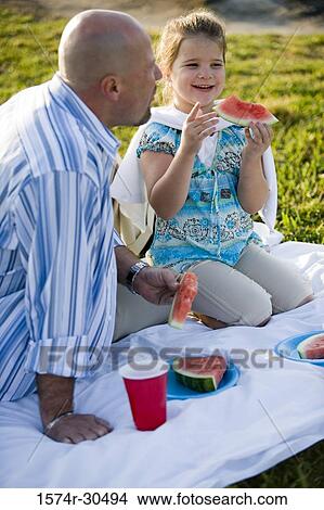 Father and daughter sitting on a blanket and eating watermelon View Large Photo Image Picture - Father and daughter sitting on a blanket and eating watermelon. Fotosearch