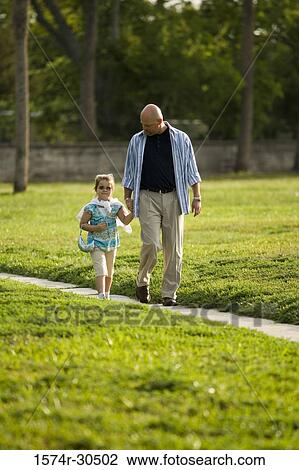 Stock Image - Father and daughter walking on a pathway at a park. Fotosearch