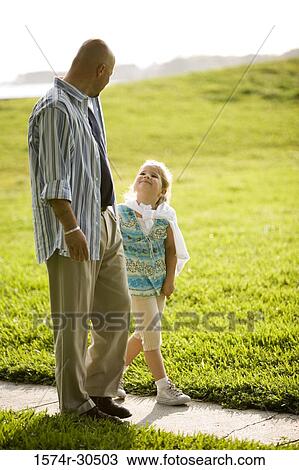 Stock Image - Father and daughter walking on a pathway at a park. Fotosearch