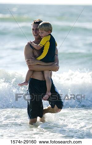Stock Image - Father carrying son in water at the beach. Fotosearch