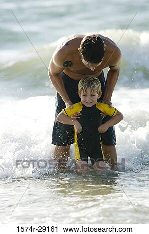 Stock Image - Father holding his son in water at the beach. Fotosearch