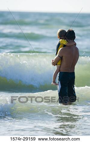 Father holding son in water at the beach View Large Photo Image Stock Photo - Father holding son in water at the beach. Fotosearch