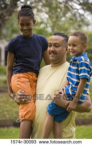 Stock Image - Father holding their children at park. Fotosearch