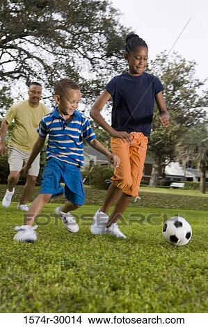 Picture - Father playing soccer ball with their children at park. Fotosearch