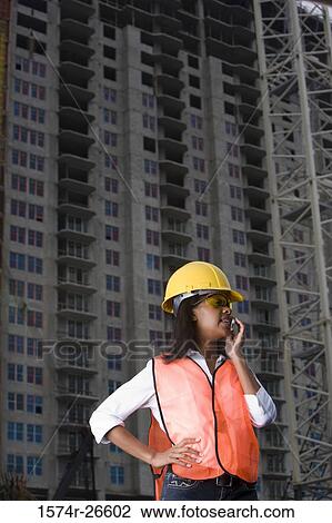 Female architect communicating on mobile phone in front of building under construction site View Large Photo Image Stock Image - Female architect communicating on mobile phone in front of building under construction site. Fotosearch