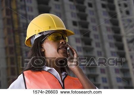 Female architect communicating on mobile phone in front of a building under construction View Large Photo Image Stock Image - Female architect communicating on mobile phone in front of a building under construction. Fotosearch