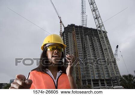 Stock Photography - Female architect communicating on walkie-talkie in front of a building under construction. Fotosearch