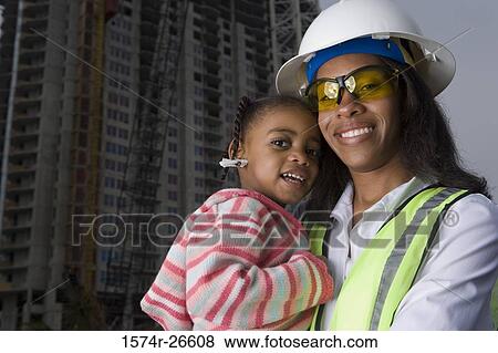 Stock Photo - Female architect holding her daughter in front of a building under construction. Fotosearch