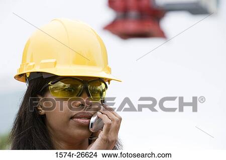 Picture - Female architect wearing hard hat and communicating on mobile phone. Fotosearch