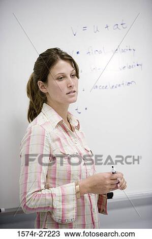 Stock Image - Female student standing in front of a white board in the classroom. Fotosearch