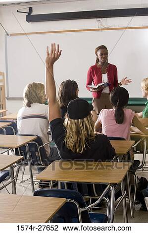 Female teacher holding book and student raising hands in the classroom View Large Photo Image Stock Image - Female teacher holding book and student raising hands in the classroom. Fotosearch