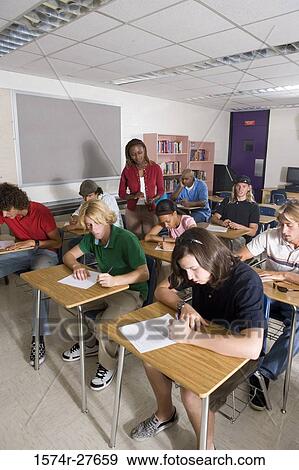 Female teacher supervising during exam in the classroom View Large Photo Image Stock Photo - Female teacher supervising during exam in the classroom. Fotosearch