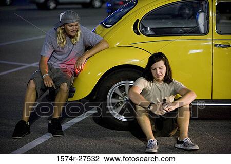 Stock Image - Friends conversing by a car at the parking area. Fotosearch