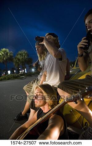 Stock Photo - Friends drinking by a car at the parking area. Fotosearch