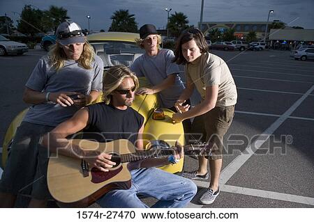 Stock Image - Friends enjoying music by a car at the parking area. Fotosearch