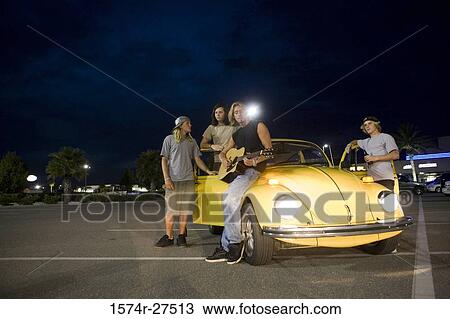 Stock Image - Friends enjoying music by a car at the parking area. Fotosearch