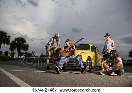 Stock Photo - Friends enjoying music by a car at the parking area. Fotosearch