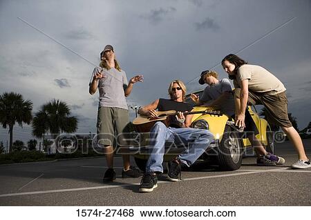 Stock Photo - Friends enjoying music by a car at the parking area. Fotosearch