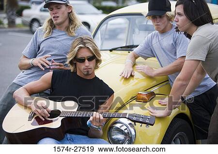 Stock Photo - Friends enjoying music by a car at the parking area. Fotosearch