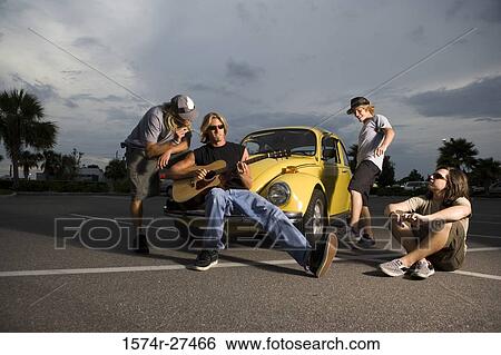 Stock Photograph - Friends enjoying music by a car at the parking area. Fotosearch