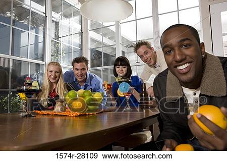 Friends enjoying their drinks and fruits in dining room View Large Photo Image Stock Photo - Friends enjoying their drinks and fruits in dining room. Fotosearch
