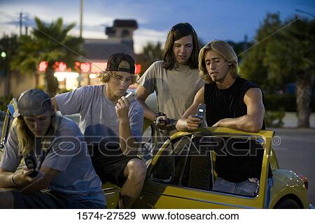 Stock Photo - Friends looking mobile phones by a car at the parking area. Fotosearch