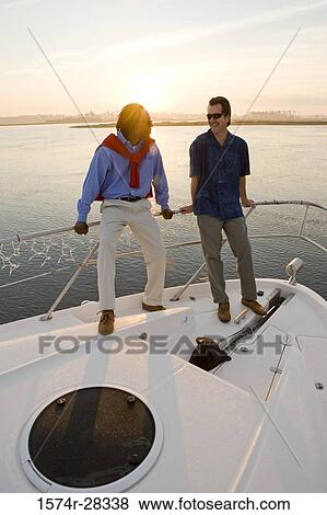 Friends standing at bow of a boat with sunset in the background View Large Photo Image Stock Photo - Friends standing at bow of a boat with sunset in the background. Fotosearch