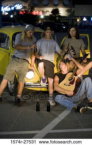 Stock Image - Friends using mobile phones and playing guitar by a car at the parking area. Fotosearch