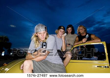 Friends using mobile phones by a car at the parking area View Large Photo Image Stock Photo - Friends using mobile phones by a car at the parking area. Fotosearch