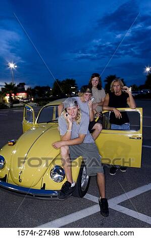 Stock Photo - Friends using mobile phones by a car at the parking area. Fotosearch