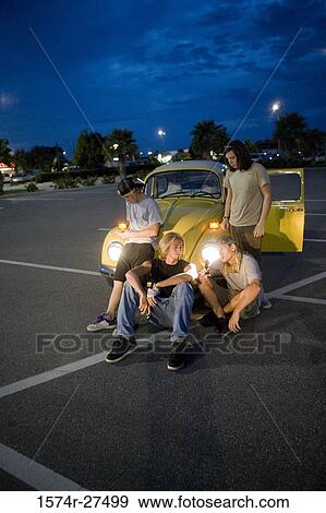Friends using mobile phones by a car at the parking area View Large Photo Image Stock Photo - Friends using mobile phones by a car at the parking area. Fotosearch