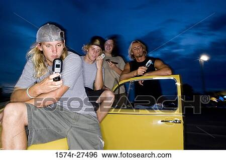 Friends using mobile phones by a car at the parking area View Large Photo Image Stock Photograph - Friends using mobile phones by a car at the parking area. Fotosearch