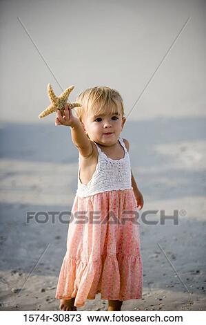 Girl holding starfish and standing on the beach View Large Photo Image Stock Image - Girl holding starfish and standing on the beach. Fotosearch