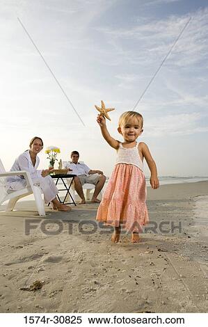 Girl holding starfish with parents sitting in the background on the beach View Large Photo Image Stock Photography - Girl holding starfish with parents sitting in the background on the beach. Fotosearch